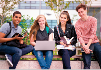 Photo of four students sitting outside on a bench collaborating on a project.